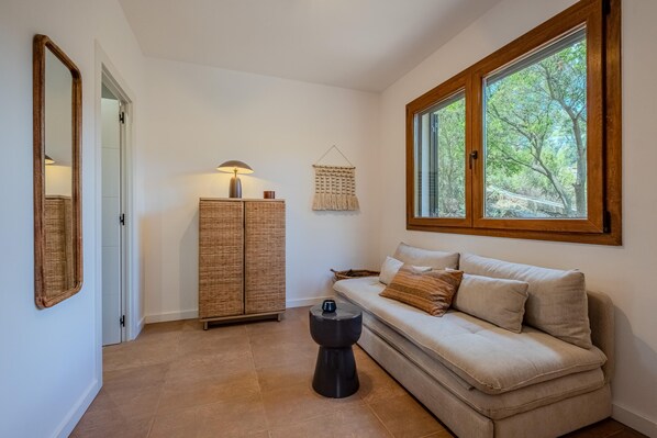 A room with a sofa, a lamp, a cabinet, a small table, and a window with a view of trees.