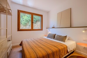 A bedroom with a bed, a window, a dresser, and a bedside table.