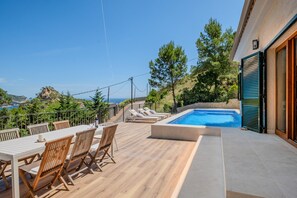 A poolside area with a table and chairs, a swimming pool, and a view of the sea.