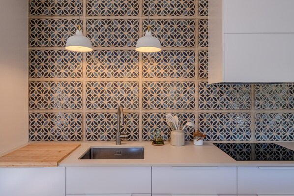 A modern kitchen with a geometric patterned backsplash, a stainless steel sink, and two pendant lights.