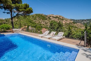 A swimming pool with lounge chairs, a wooden deck, and a view of a mountainous landscape.