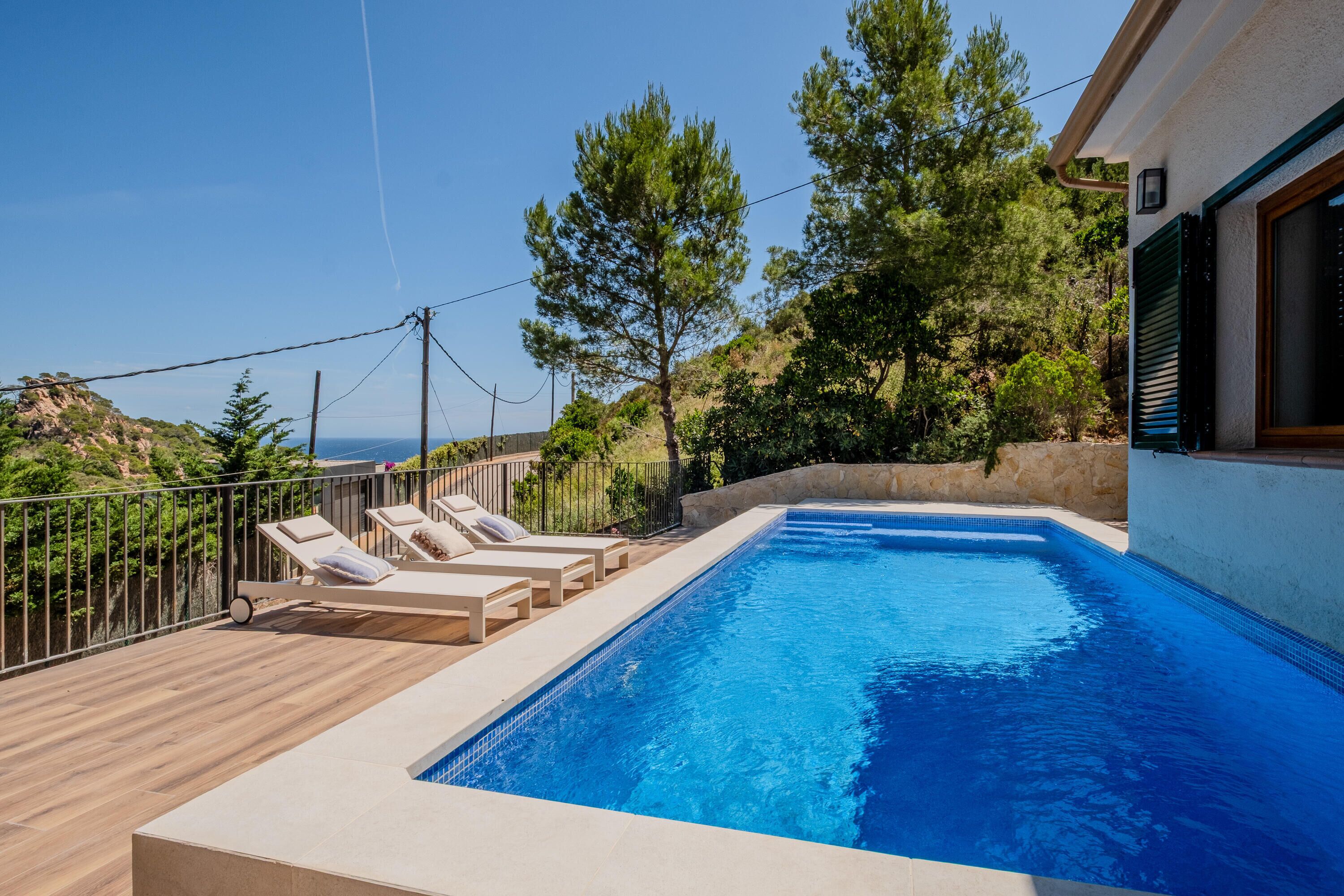 Une piscine entourée d’arbres, avec des chaises longues et une vue sur le paysage.