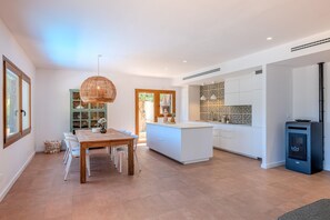 A modern kitchen with white cabinetry, a central island, and a dining area with a wooden table and chairs.