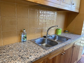 A kitchen with two stainless steel sinks, a granite countertop, wooden cabinets, and a green basket. - AJ-17 Apartment near the center, large community with pool (Calella de Palafrugell)