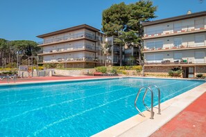 A swimming pool with a red border, adjacent to a multi-story building with balconies and a stone facade. - AJ-17 Apartment near the center, large community with pool (Calella de Palafrugell)