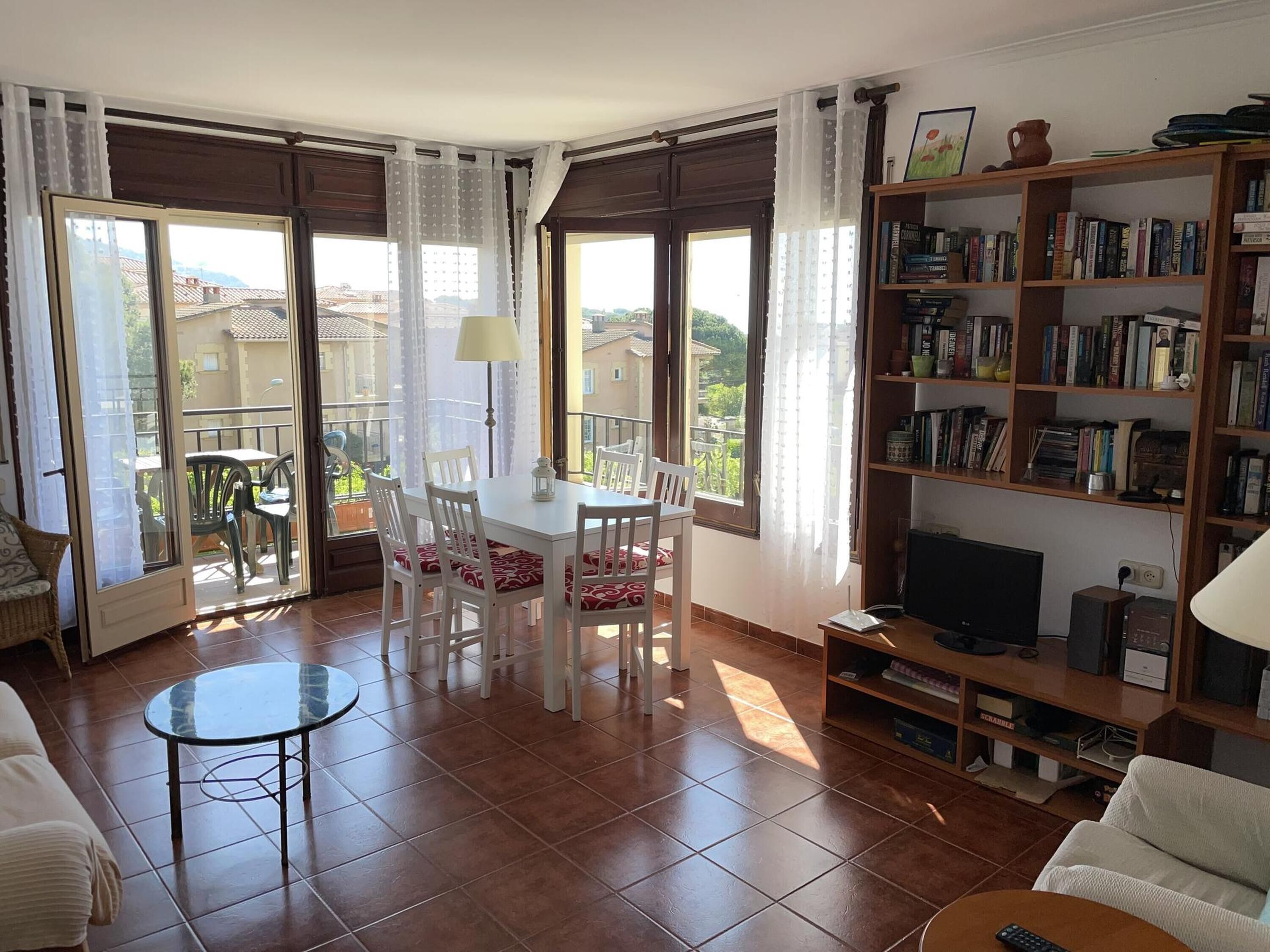 A living room with a dining area, a bookshelf, a TV, and a balcony with a view.
