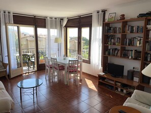 A living room with a dining area, a bookshelf, a TV, and a balcony with a view. - AJ-17 Apartment near the center, large community with pool (Calella de Palafrugell)