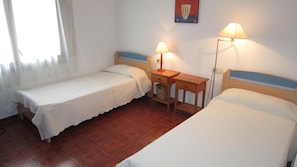 A room with two single beds, a small wooden table with a lamp, and a window with curtains. - AJ-17 Apartment near the center, large community with pool (Calella de Palafrugell)