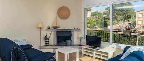 A living room with a fireplace, a television, and a large window with a view of the neighborhood.