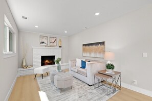 Ein modernes Wohnzimmer mit Kamin, weißen Wänden und einem Sofa mit blauem Kissen.