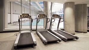 Tres cintas de correr en un gimnasio moderno con amplios ventanales con vistas a una piscina.