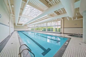 An indoor swimming pool with clear glass ceilings, a tiled floor, and a view of greenery outside. - Luxury 28th-Floor Downtown Haven, Skyline Views, Five-Star Amenities & Location (Vancouver)
