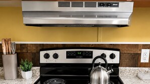 Una cocina con estufa negra, extractor de acero inoxidable y un reloj marcando las 5:12.