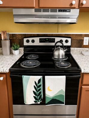 A kitchen with a black stove, a stainless steel range hood, and a clock displaying 5:12. - New! Hot Tub, Fire Pit, Spacious, Great Location, Relaxing, BBQ, Fire Pit (Fayetteville)