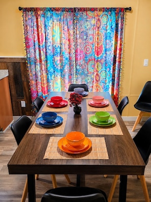 Une table à manger dressée avec des assiettes colorées et un vase rempli de fleurs, le tout surmonté d’un rideau aux couleurs vives.