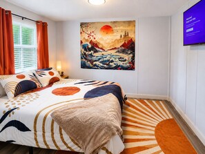 Une pièce avec un lit, un téléviseur fixé au mur, un tableau et une fenêtre avec des rideaux.
