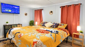 Un dormitorio con una cama grande, un televisor instalado en la pared, una mesita de noche con una lámpara y una planta.