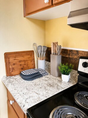 Una cocina con encimeras de granito, una tabla de cortar de madera, una olla blanca con una planta y una estufa.
