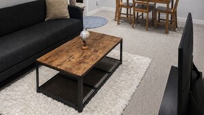 Uma sala de estar moderna com um sofá preto, mesa de centro de madeira, mesa de jantar com cadeiras, uma TV e um mapa-múndi na parede.