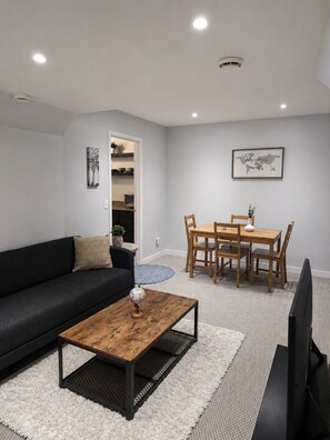 A modern living room with a black sofa, wooden coffee table, dining table with chairs, a TV, and a world map on the wall.