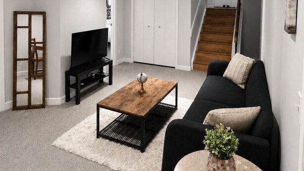 Uma sala de estar moderna com um sofá preto, uma mesa de centro de madeira, uma televisão e uma escada que leva a outro andar.