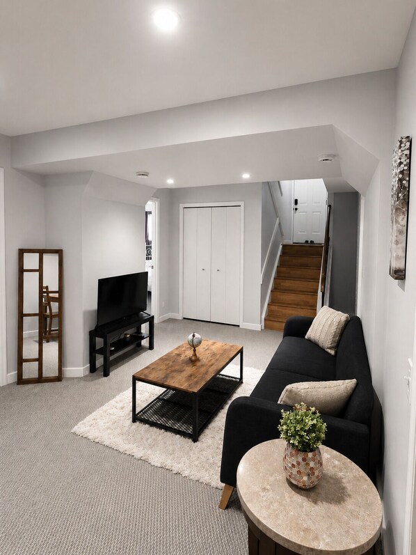 A modern living room with a black sofa, a wooden coffee table, a TV, and a staircase leading to another level.