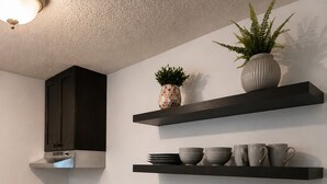 Cozinha moderna com armários escuros, forno embutido, pia e duas prateleiras com objetos decorativos.