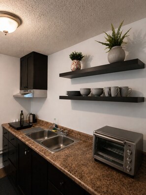 A modern kitchen with dark cabinets, a built-in oven, a sink, and two wall-mounted shelves with decorative items.