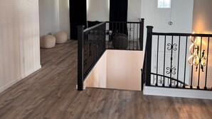 A spacious room with wooden flooring, a staircase with black railings, and a small window.