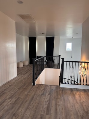 Ein geräumiges Zimmer mit Holzboden, einer Treppe mit schwarzen Geländern und einem kleinen Fenster.
