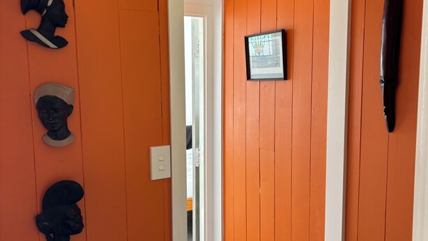 A hallway with orange walls, a white door, and a framed picture on the wall. - A restorative stay where the mighty Waikato awa meets the Tasman Sea (Port Waikato)