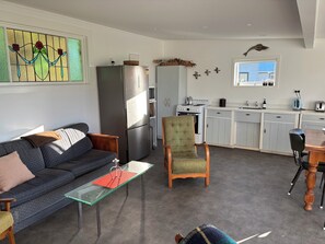 A modern kitchen with a refrigerator, stove, and sink. There is a dining table with chairs and a sofa in the living area.