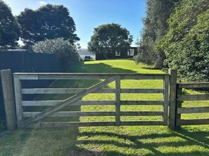 A wooden gate leading to a grassy area with a building in the background.