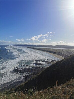 A coastal landscape with a beach, ocean waves, and distant hills under a clear sky. - A restorative stay where the mighty Waikato awa meets the Tasman Sea (Port Waikato)