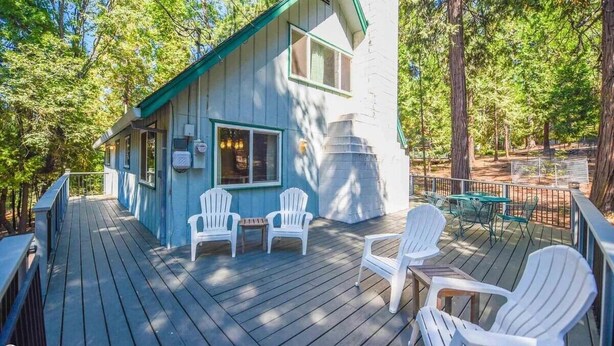 Une terrasse en bois, avec des chaises blanches et une table, entourée d’arbres.
