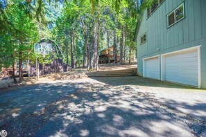 A residential property with a two-car garage, a basketball hoop, and a house surrounded by tall trees.