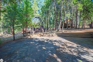 A forested area with a basketball court, a wooden structure, and a building with a sloped roof.