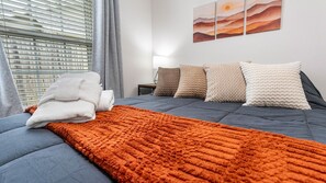 Habitació d'hotel amb un llit, una manta, almoinades, una taula de nit i una paret amb obra d'art.