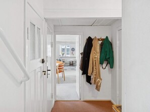 Un couloir avec un porte-manteau, une porte et, au fond, on aperçoit une pièce avec une table et des chaises.