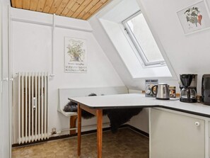 Une petite cuisine avec un plan de travail blanc, une machine à café, une bouilloire et un radiateur.