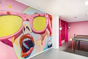 Ein Zimmer mit einem lebendigen Wandgemälde, einem Tischtennisplatte und einer rosafarbenen Wand.