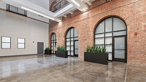 A spacious lobby with a polished concrete floor, large arched windows, and brick walls.