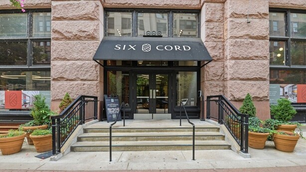 A building entrance with a black awning labeled 'SIX CORD,' steps leading up to the door, and potted plants on either side.