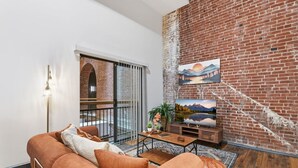 A living room with a brick wall, a sofa, a TV, and a balcony with a view.