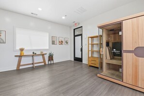 A modern room with a wooden floor, a whiteboard, a wooden desk with a vase and plants, a glass cabinet with a logo, and a black door. - 1BR Loft | Full Amenity Access in Downtown St. Louis (St. Louis)