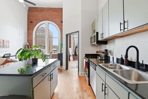 A modern kitchen with a central island, stainless steel appliances, and a view of a cityscape through a large arched window.