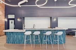 A modern kitchen with a central island, bar stools, and a brick wall. - 1BR Loft | Downtown STL + Rooftop, Sauna, Firepit (St. Louis)