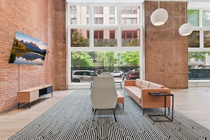 Un intérieur moderne avec un mur en briques, une grande fenêtre, un canapé, un fauteuil, un téléviseur et des luminaires suspendus.