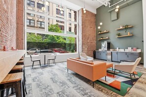 A modern interior with a dining area, seating, kitchen, and large windows overlooking a street. - 1BR Loft | Downtown STL + Rooftop, Sauna, Firepit (St. Louis)
