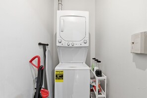Une petite buanderie blanche, équipée d’un lave-linge, d’un tuyau et d’un distributeur de lessive.